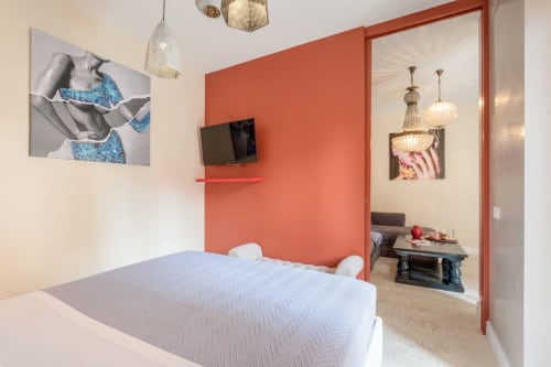 Camera moderna alle Petra Apartments Roma con letto bianco, parete accent color corallo, TV e soggiorno adiacente con lampada sospesa