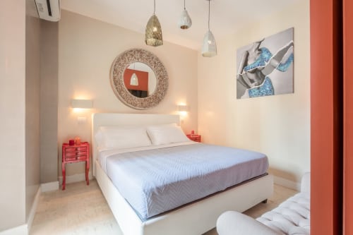 Camera moderna presso Petra Apartments Roma con letto bianco, comodino rosso, lampade a sospensione e specchio decorativo circolare
