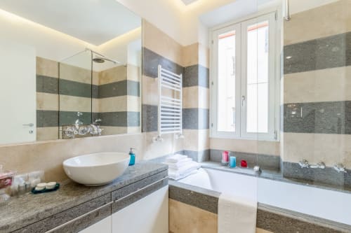 Moderno bagno di Petra Apartments Rome con piastrelle a righe, lavabo ovale, vasca, doccia e scaldasalviette