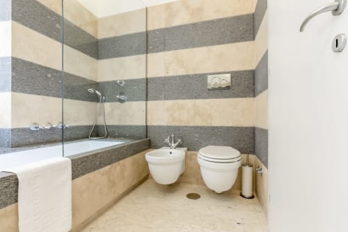Moderno bagno di Petra Apartments Rome con piastrelle a righe, doppi WC, bidet e doccia con box in vetro