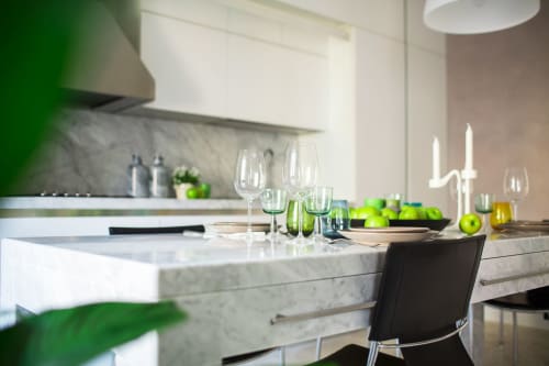 Area living-cucina moderna degli Apartments Petra Roma con piano marmo, mele verdi, calici di vino e mobili bianchi