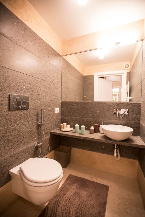 Bagno moderno negli Appartamenti Petra Roma con piastrelle marroni, lavabo bianco, toilette, doccia e candele decorative