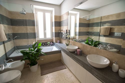 Bagno moderno presso Petra Apartments a Roma con doppi lavandini, vasca, piastrelle a righe e piante verdi