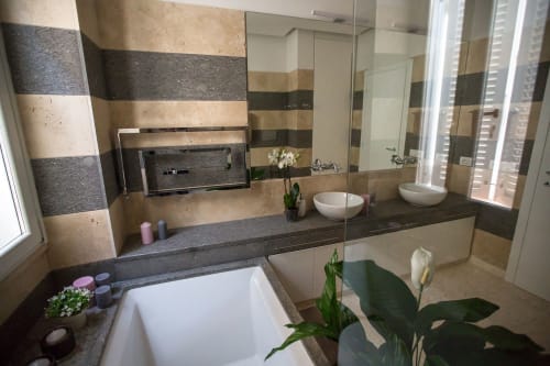 Bagno moderno in appartamento romano con doppio lavabo, vasca, piastrelle a righe e luce naturale dalle finestre