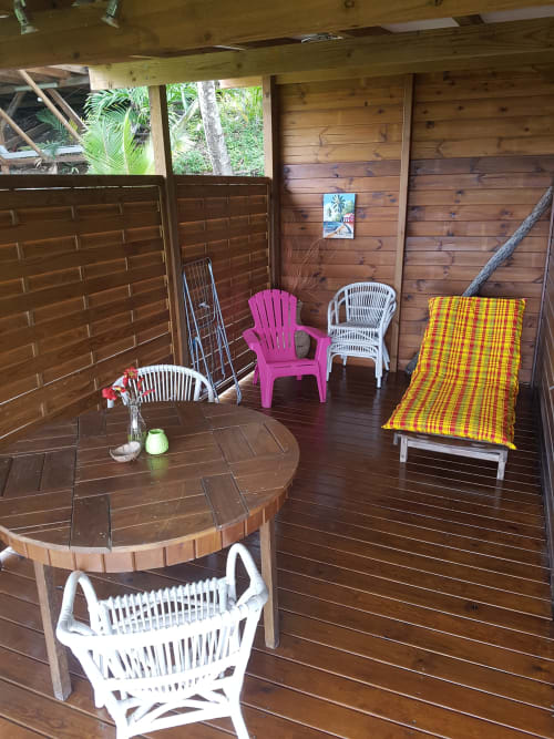 Terrasse de cottage aux Hauts De Deshaies avec chaises colorées, table ronde et mobilier de détente surplombant Deshaies