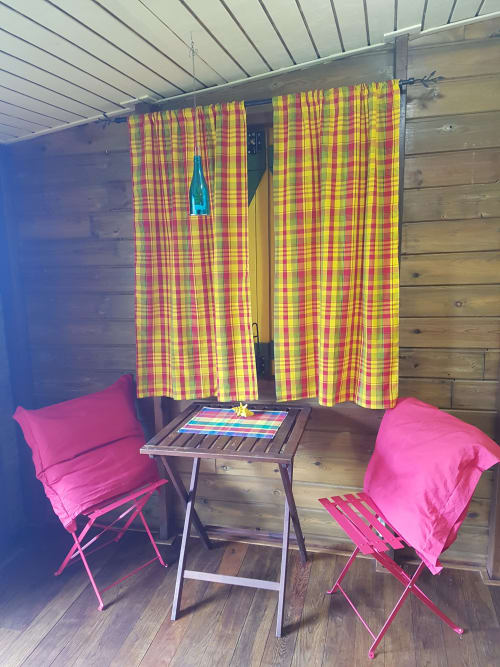 Terrasse colorée aux Hauts De Deshaies avec chaises roses, rideaux à carreaux et terrasse en bois à Deshaies