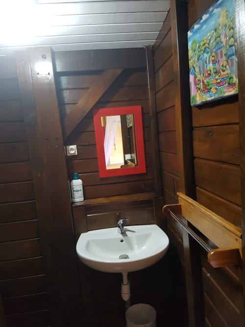 Salle de bain de la villa Les Hauts De Deshaies avec lavabo sur pied blanc, miroir à cadre rouge et murs en bois, Deshaies Guadeloupe