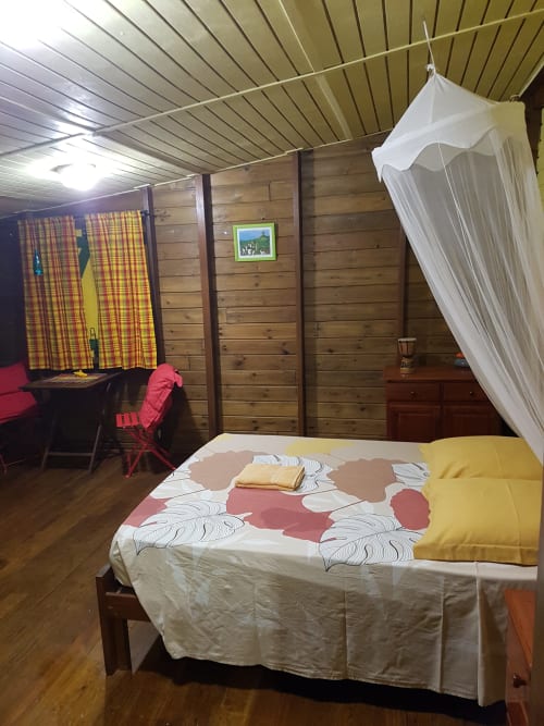 Chambre cosy de la maison d'hôtes Les Hauts De Deshaies avec lit, moustiquaire, murs en bois et décor coloré à Deshaies