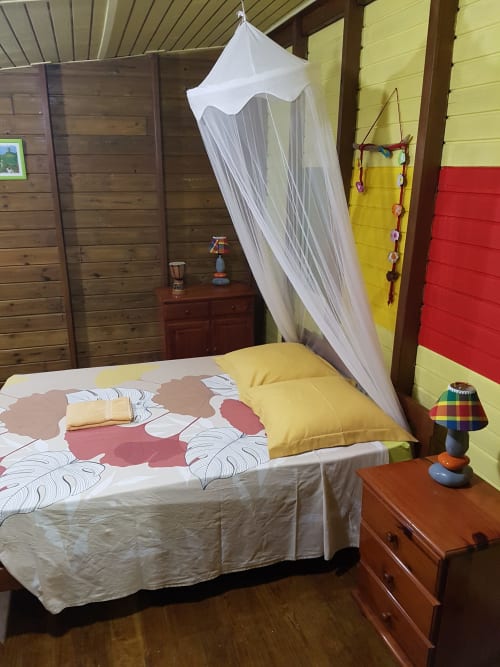 Chambre colorée aux Hauts de Deshaies avec lit à baldaquin, murs jaunes et décor tropical à Deshaies, Guadeloupe