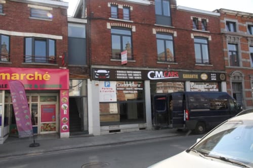 Veduta della strada di Courcelles con vetrina CM Cars e edifici in mattoni sopra i negozi