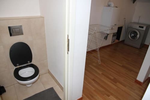 Bathroom with black toilet seat and laundry room with washing machine at Appartements Courcelles apartment in Courcelles