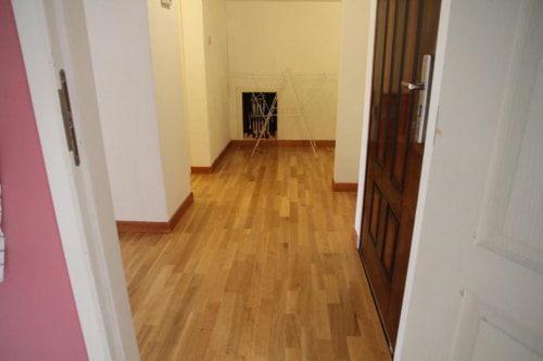 Wooden hallway in Courcelles apartment with white walls, pink door, brown wooden doors, and framed artwork on yellow wall