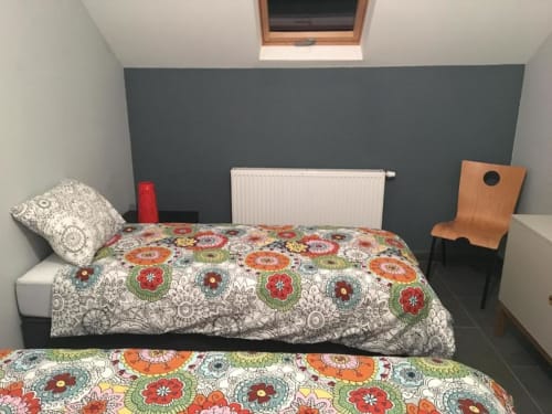 Quarto aconchegante do apartamento Courcelles com roupa de cama estampada colorida, parede de destaque cinza, radiador e cadeira de madeira