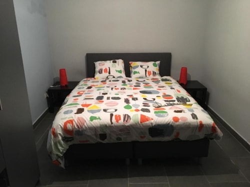 Quarto moderno no apartamento Courcelles com estrutura de cama preta, roupa de cama estampada com comida colorida, lâmpadas vermelhas e paredes brancas