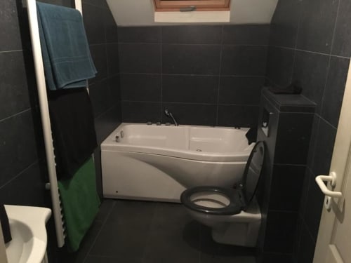 Banheiro moderno com azulejos pretos, banheira e vaso sanitário brancos nos Appartements Courcelles, Courcelles