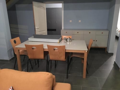 Sala de jantar moderna com mesa de madeira, cadeiras laranja, armários de cozinha e paredes azuis em Appartements Courcelles