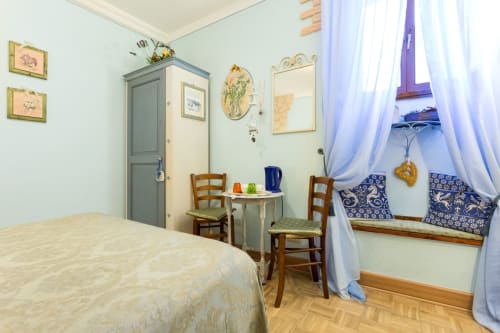 Camera accogliente del B&B Assisi con letto, sedie in legno, finestra con cuscini blu e pareti azzurre