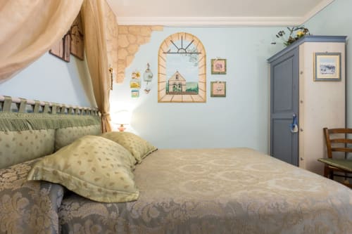 Camera accogliente presso Dormire Assisi B&B con pareti azzurre, letto a baldacchino, finestra rustica e armadio.