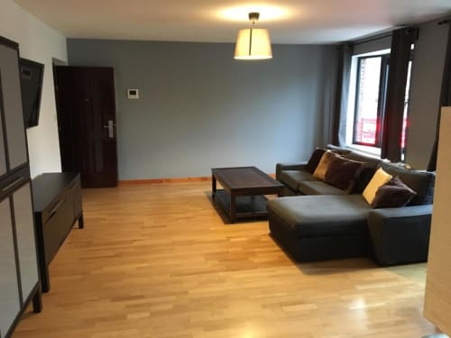 Modern apartment living room with dark leather sofa, wooden floors, flat-screen TV, and city views at Courcelles hotel