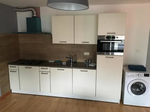 Modern kitchen in Courcelles apartment with white cabinetry, gas stove, oven, and washing machine