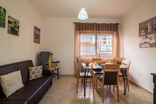 Bright apartment dining and living area with table seating, dark sofa, and city view at Armação Beach Residences, Portugal