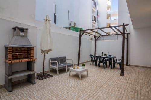 Shared terrace at Armação Beach Residences with brick fireplace, seating, pergola, and dining area overlooking city