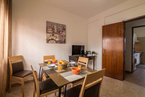 Dining area in T2 apartment at Armação Beach Residences with table, wooden chairs, TV, and kitchen access