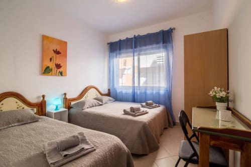 Bright twin bedroom at Armação Beach Residences with wooden beds, blue curtains, desk, and city view in Armação de Pêra