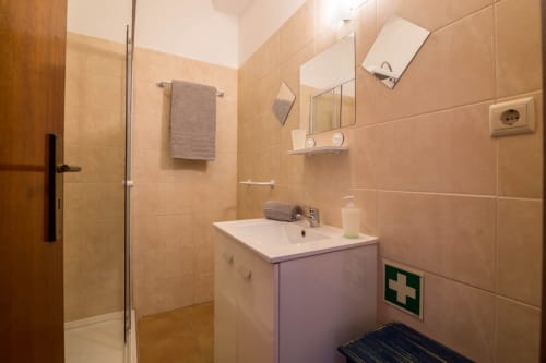 Modern bathroom with beige tiles, white sink vanity, glass shower enclosure, and first aid kit at Armação Beach Residences,