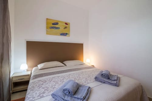 Modern bedroom at Armação Beach Residences with brown headboard, white pillows, rolled towels, bedside lamp, and yellow