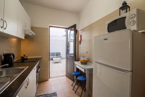 Modern kitchenette with white cabinets, dark countertop, appliances, and blue bar stools at Armação Beach Residences, Armação