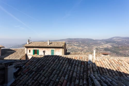 Tradizionale B&B in pietra con persiane verdi affacciato sulla campagna di Assisi e sulle dolci colline umbre sotto un cielo azzurro