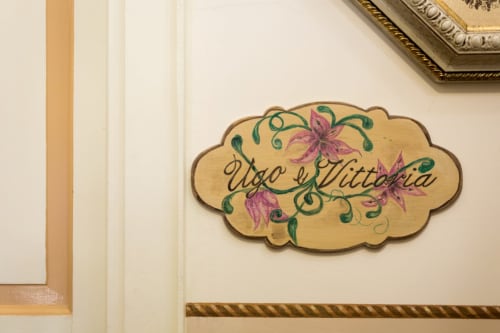 Cartello decorativo in legno della Camera Ugo e Vittoria al Dormire Assisi B&B ad Assisi, Italia con fiori rosa e viti verdi