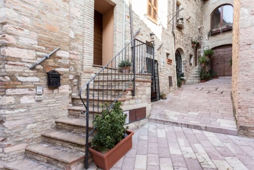 Storico cortile in pietra con scale e portali ad arco nella B&B di Assisi, con architettura tradizionale e piante in vaso