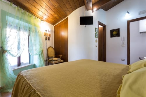 Accogliente camera da letto al Dormire Assisi B&B con biancheria gialla, soffitto in legno, tende verdi e TV