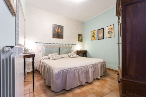 Camera luminosa del B&B di Assisi con letto matrimoniale, pareti azzurre, opere floreali, pavimenti in legno e arredi tradizionali