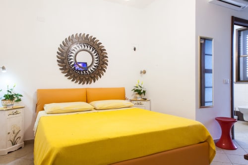 Camera da letto luminosa con biancheria gialla, testata arancione e specchio dorato decorativo presso l'Affittacamere Al Mare a Torre Grande