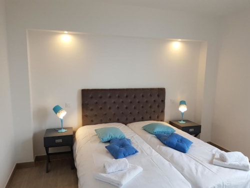 Chambre moderne à la Résidence Lésia à Corbara avec lits jumeaux, tête de lit sombre, oreillers bleus, tables de nuit avec lampes turquoise, et