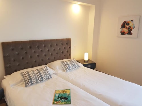 Chambre moderne à la Résidence Lésia à Corbara avec tête de lit capitonnée, lits jumeaux, oreillers à motifs et lampe de chevet