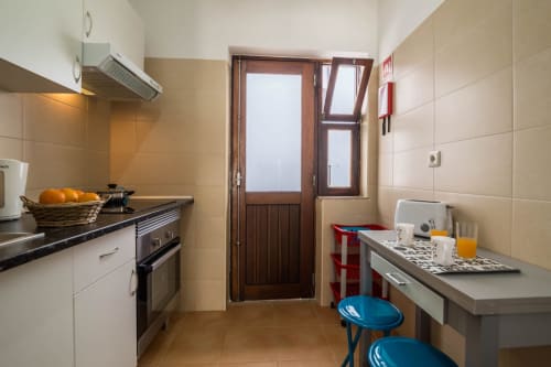 Modern kitchen and dining area in Armação Beach Residences apartment with tiled floors, white cabinetry, and blue stools