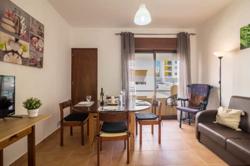 Armação Beach Residences apartment dining area with wooden table, brown leather sofa, city view balcony, and modern amenities