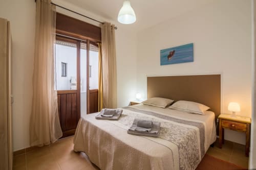 Bright bedroom at Armação Beach Residences with double bed, wooden headboard, balcony doors, and coastal artwork in Armação