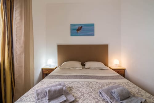 Bedroom at Armação Beach Residences with queen bed, brown headboard, bedside lamps, and beach artwork in Armação de Pêra