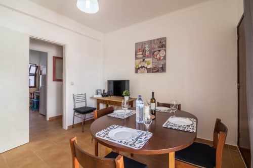 Dining area in T2 apartment at Armação Beach Residences with round table, wooden chairs, and kitchenette view
