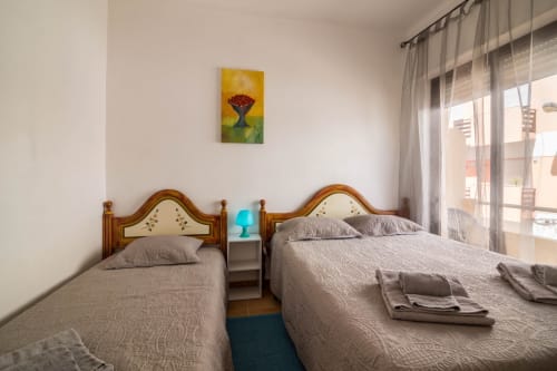 Twin bedroom at Armação Beach Residences with wooden headboards, city views through balcony doors, and modern amenities