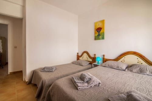 Bright twin bedroom at Armação Beach Residences with wooden headboards, terracotta floors, and colorful flower artwork