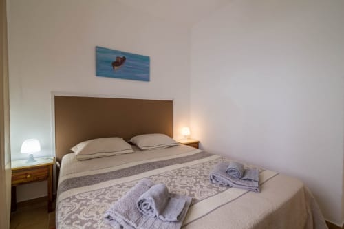 Cozy bedroom at Armação Beach Residences with queen bed, brown headboard, bedside lamps, and coastal artwork in Armação de