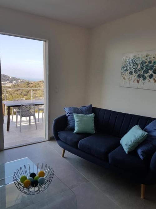 Séjour moderne à la Résidence Lésia à Corbara avec vue mer, canapé bleu marine et balcon sur les collines