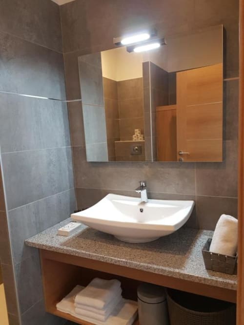 Salle de bain moderne à la Résidence Lésia à Corbara avec lavabo blanc, carrelage gris et miroir-armoire éclairé