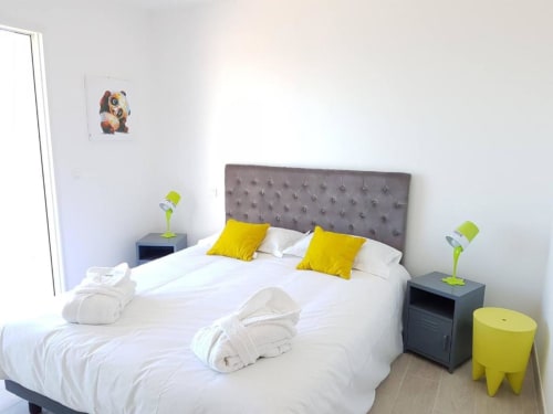 Chambre moderne à la Résidence Lésia à Corbara avec tête de lit grise, literie blanche, coussins jaunes et lampes de chevet